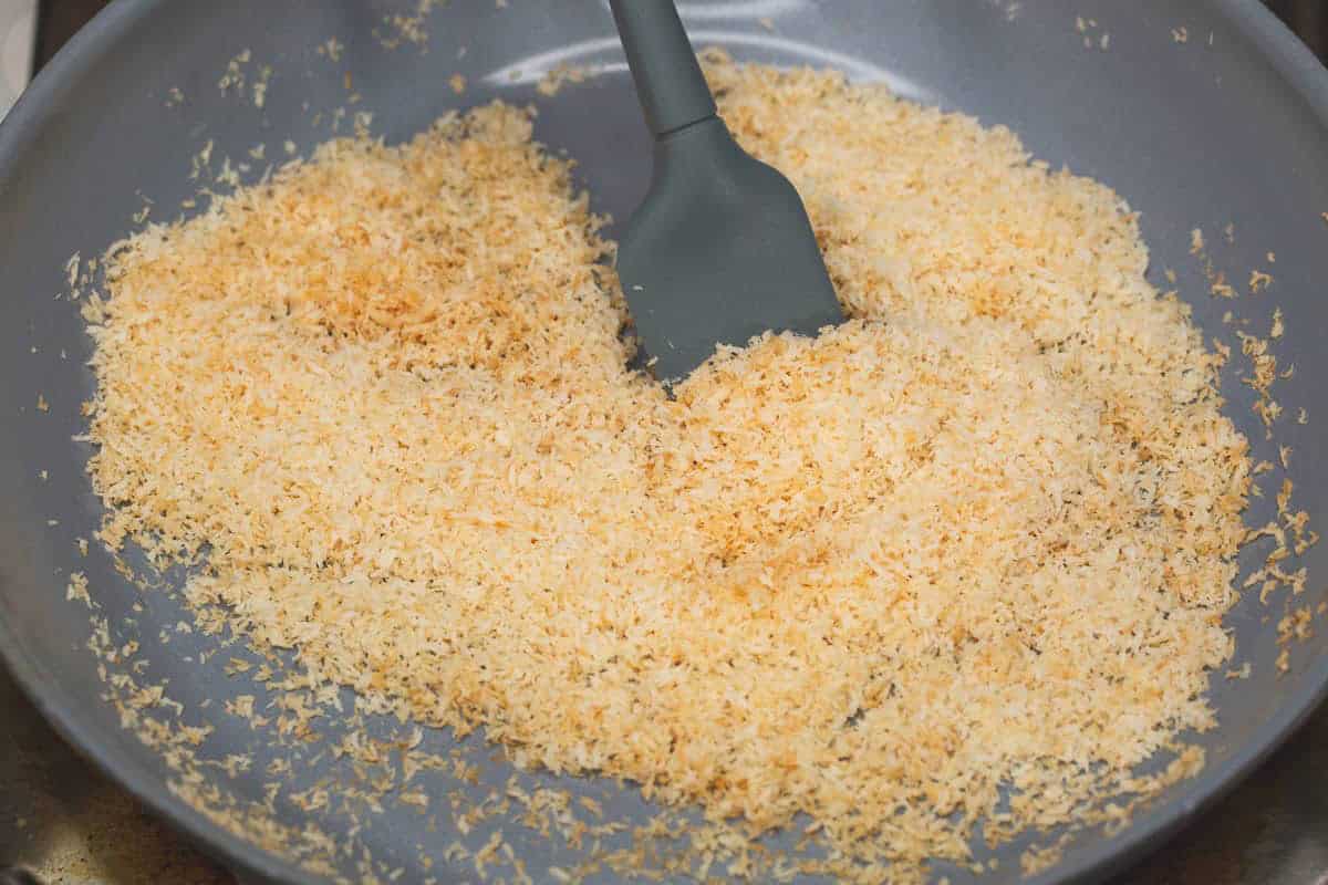 Stirring the coconut in the pan using a spatula.