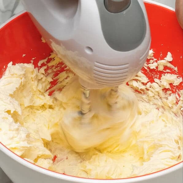 Beating the cream cheese and butter in the bowl. Beating the cream cheese mixture and powdered sugar in the bowl.