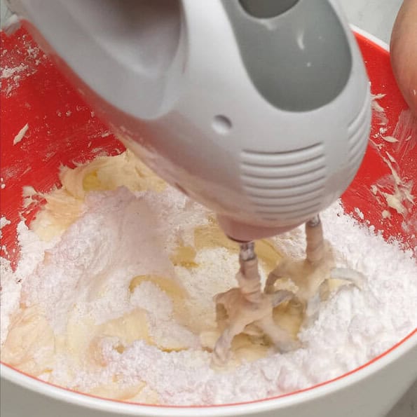 Beating the cream cheese and butter in the bowl. Beating the cream cheese mixture and powdered sugar in the bowl.